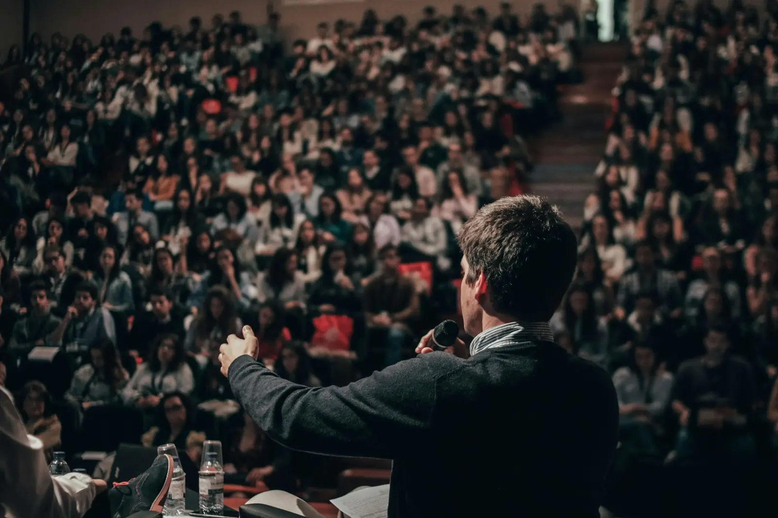 A speaker on a lit stage addressing a full conference auditorium