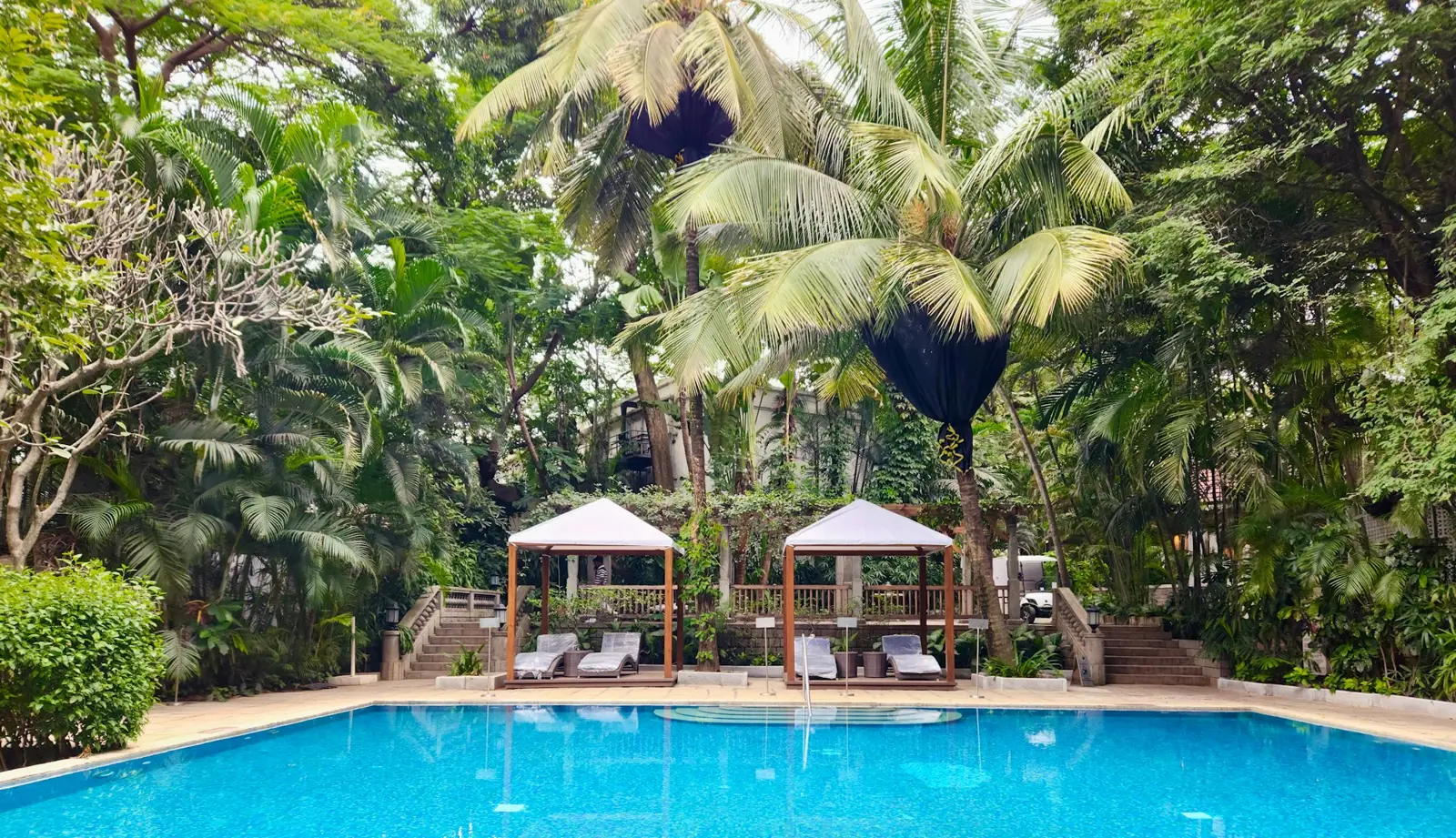 Two white cabanas beside a resort pool surrounded by palms