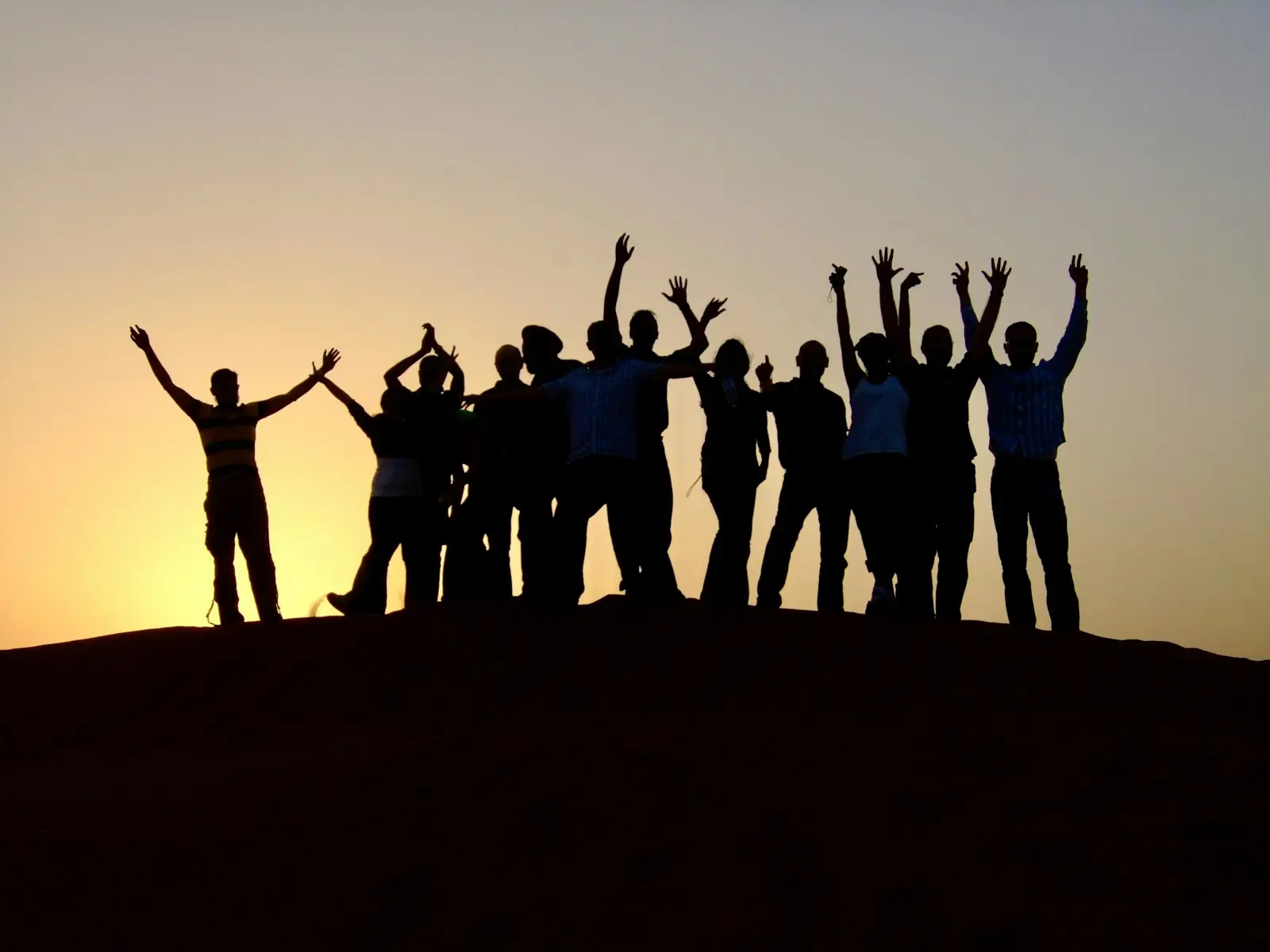 Silhouettes of a group with arms raised on a hilltop at sunset