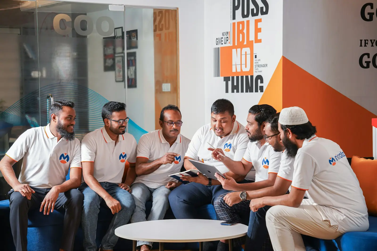 A team in matching white T-shirts reviewing plans together in a bright office lounge