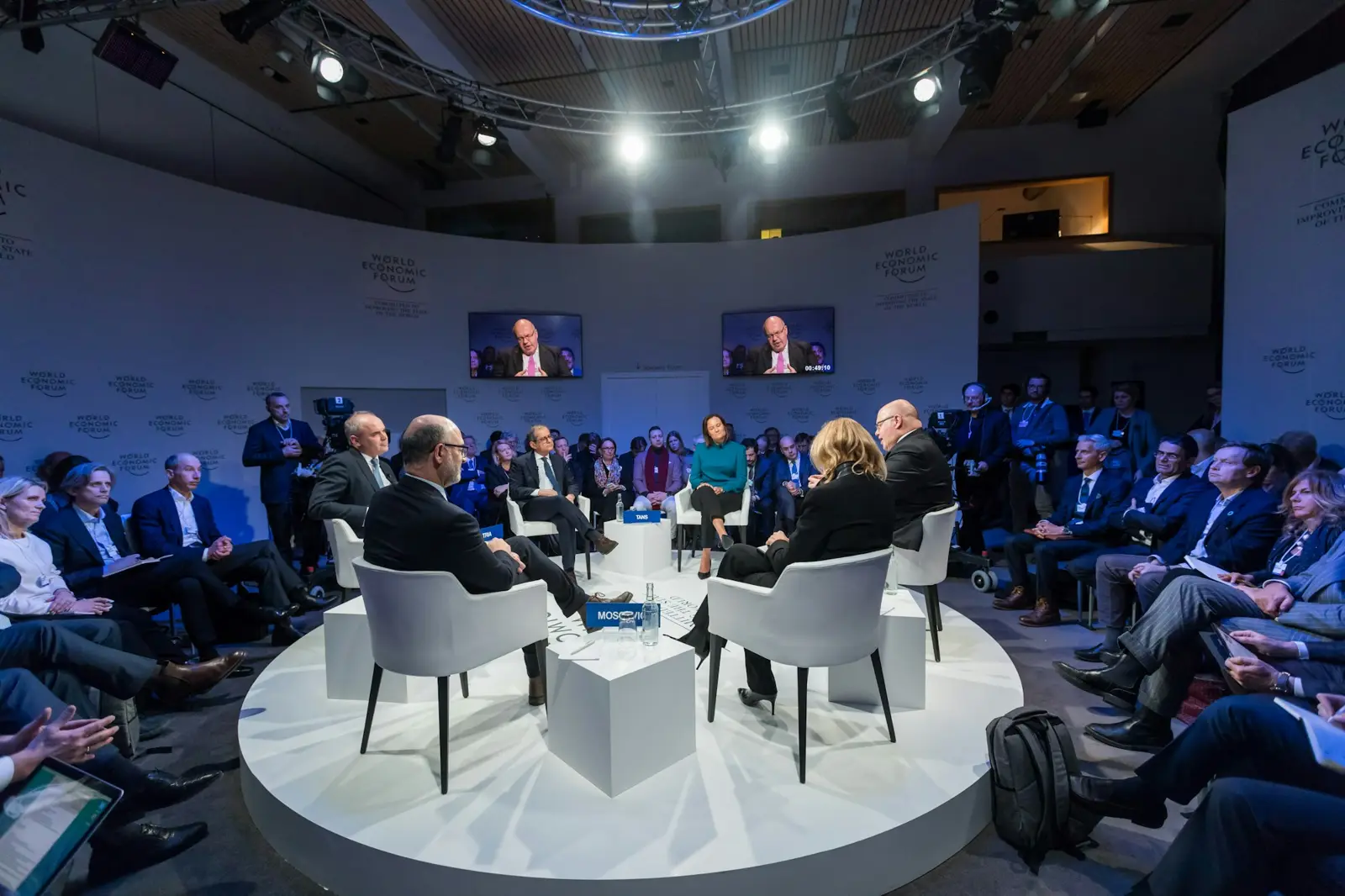 A panel discussion on a round white stage with an audience seated around it